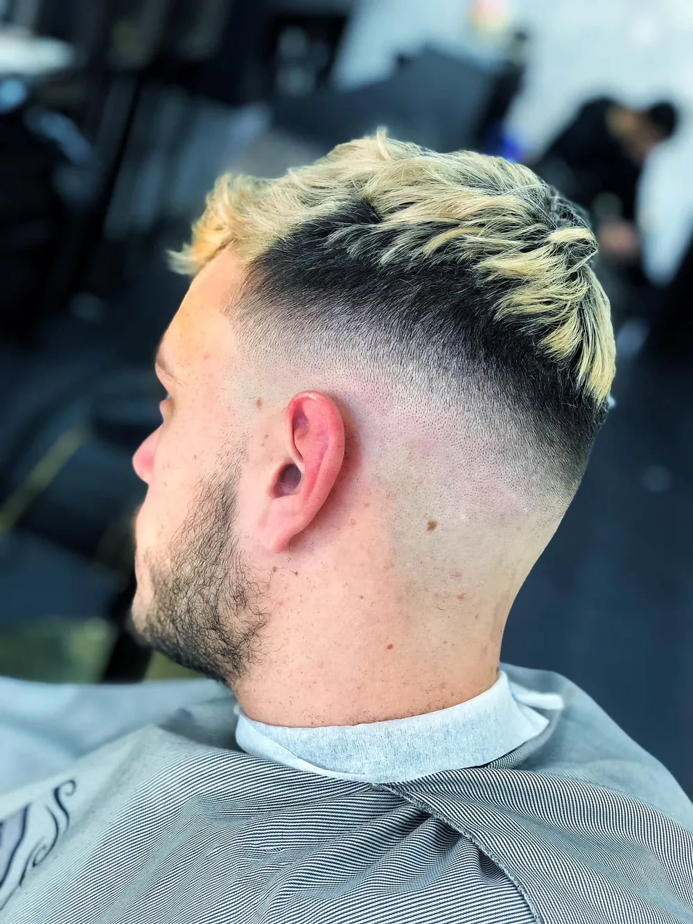 Heren skin fade met getextureerde, licht geblondeerde coupe, zij-achteraanzicht