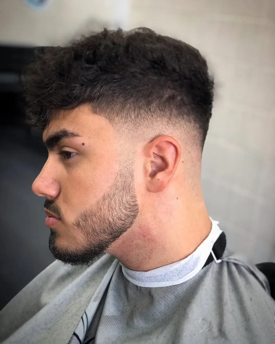 Krullende coupe met mid skin fade en strak afgewerkte baardlijn, zijprofiel