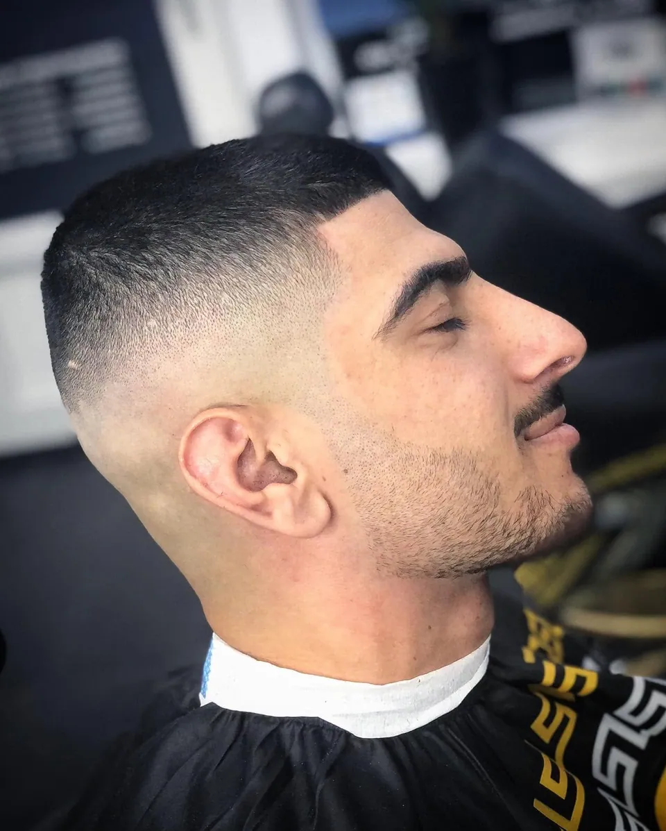 Korte buzzcut met hoge skin fade en lichte baard, zijprofiel