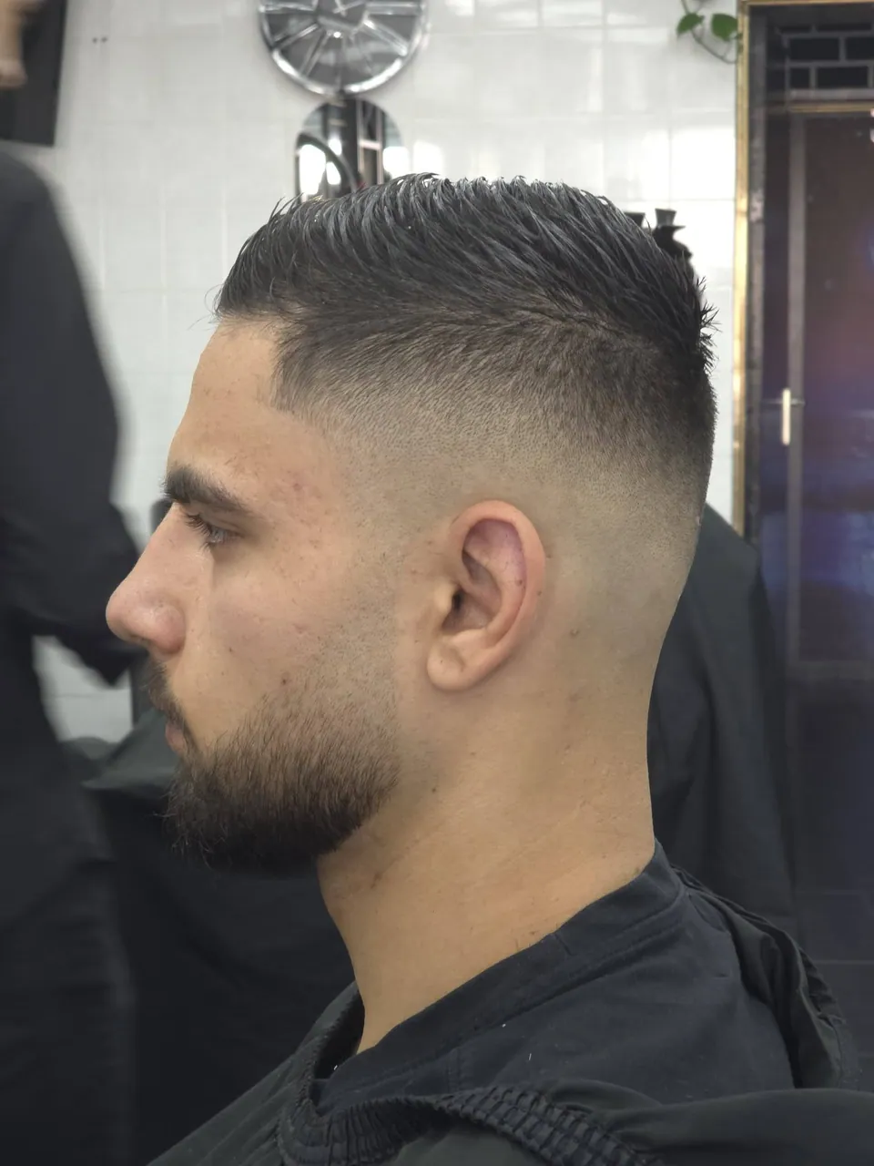 Korte getextureerde crop met hoge skin fade en baard, zijprofiel
